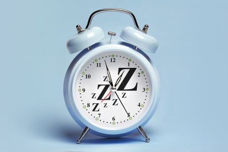 A blue alarm clock with Z's scattered around clockface, sitting on a blue background/surface
