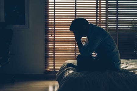 Man sitting head in hands on the bed in the dark bedroom with low light